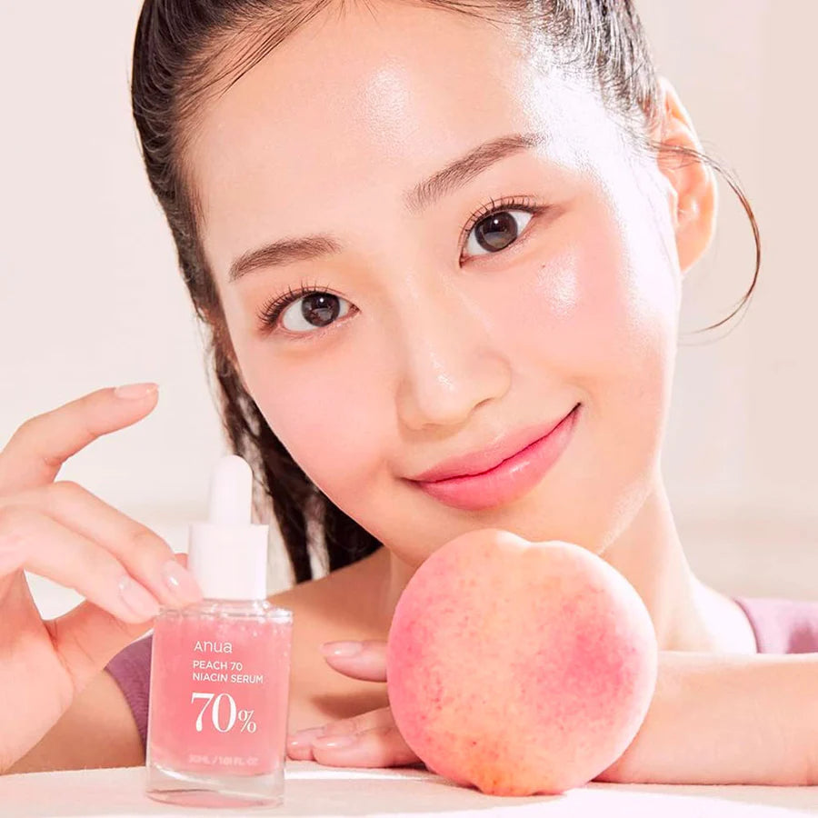 Anua 70 percent niacinamide serum bottle held by woman with glowing skin and peach fruit