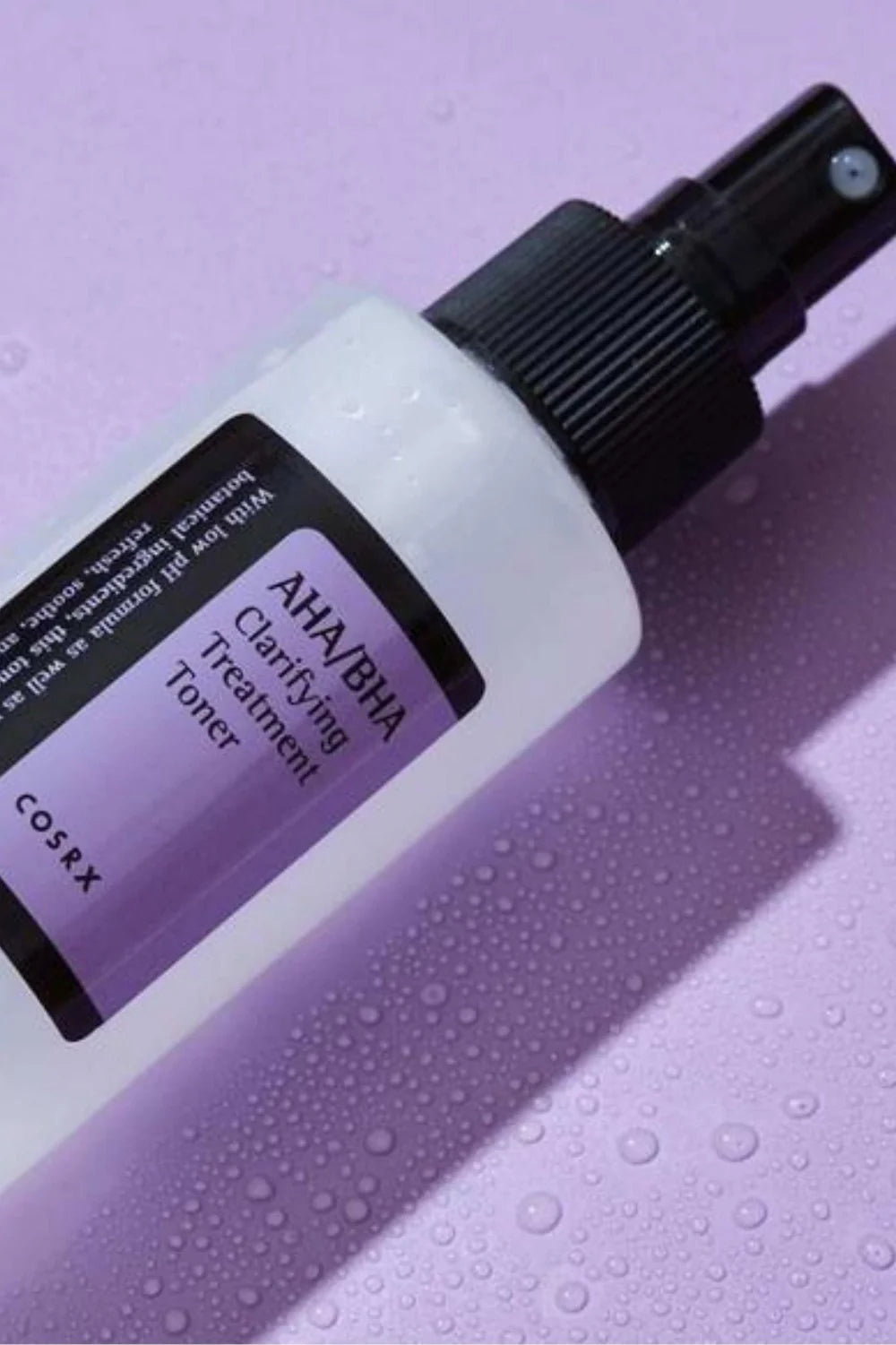 Cosrx AHA BHA toner for acne in spray bottle on a purple background with water droplets