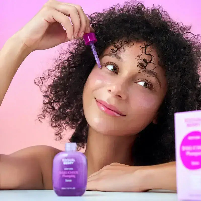 Zuzu Aura Bakuchiol Serum in a purple bottle being applied to skin for a glowing complexion