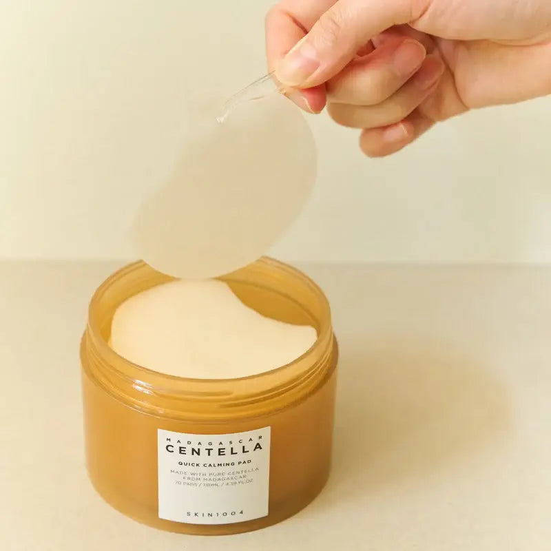 Zuzu Aura mixsoon centella toner pad in a jar, featuring a hand lifting a toner pad from the container